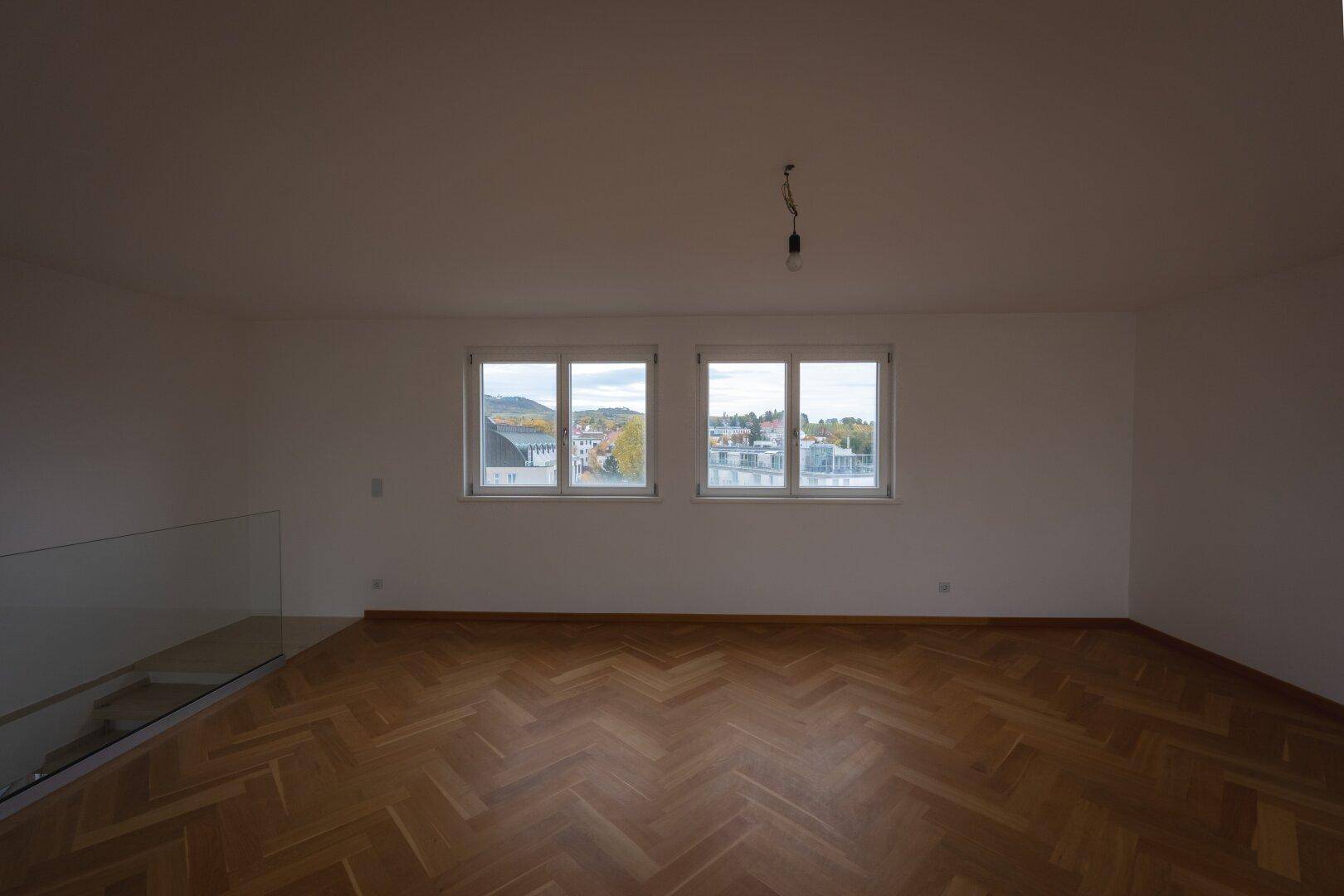 Helles Wohnzimmer mit Fischgrätparkett und weitem Blick über die Stadt und die Umgebung.