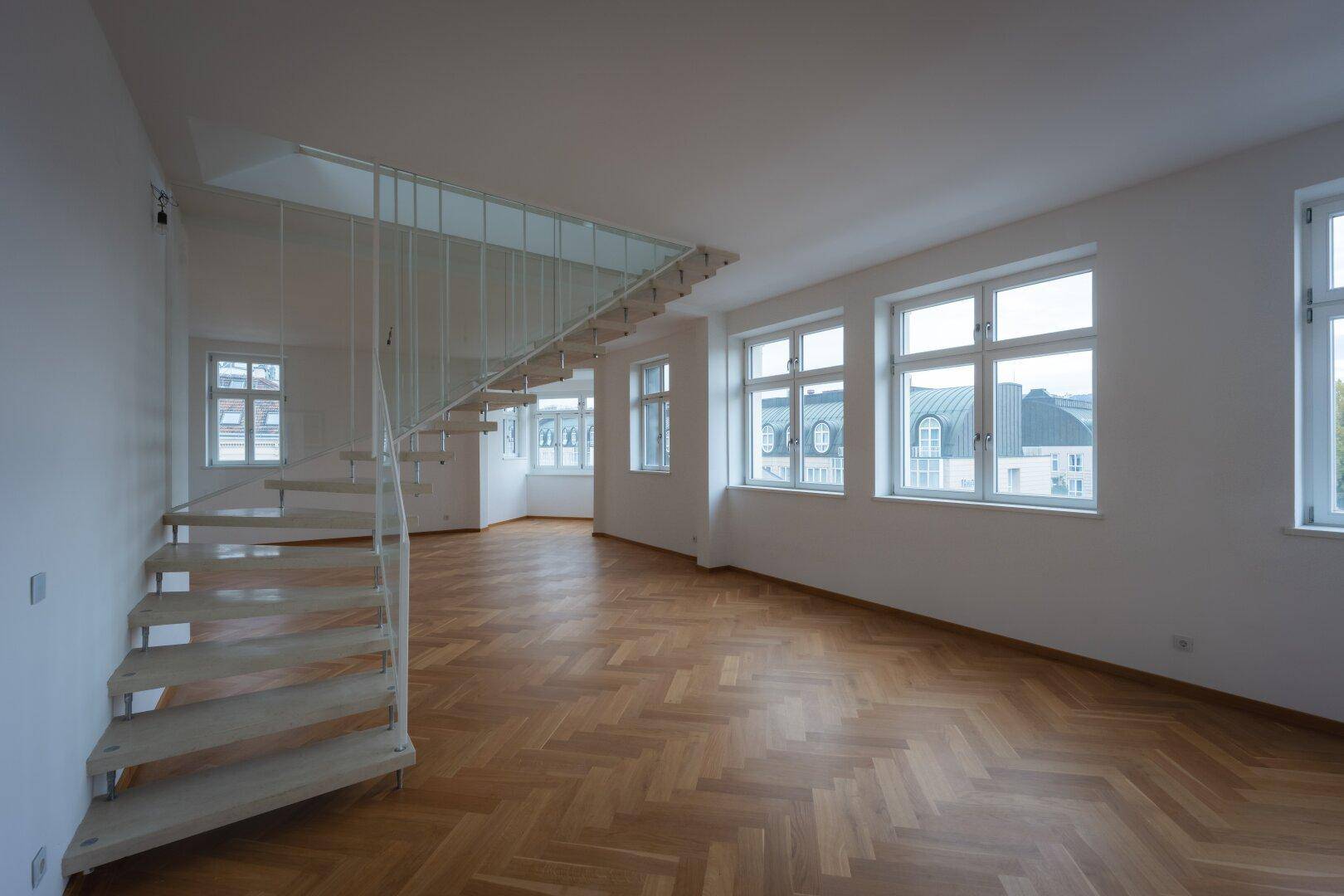 Großzügiges Wohnzimmer mit Fischgrätparkett und einer modernen Treppe, die zwei Ebenen verbindet.