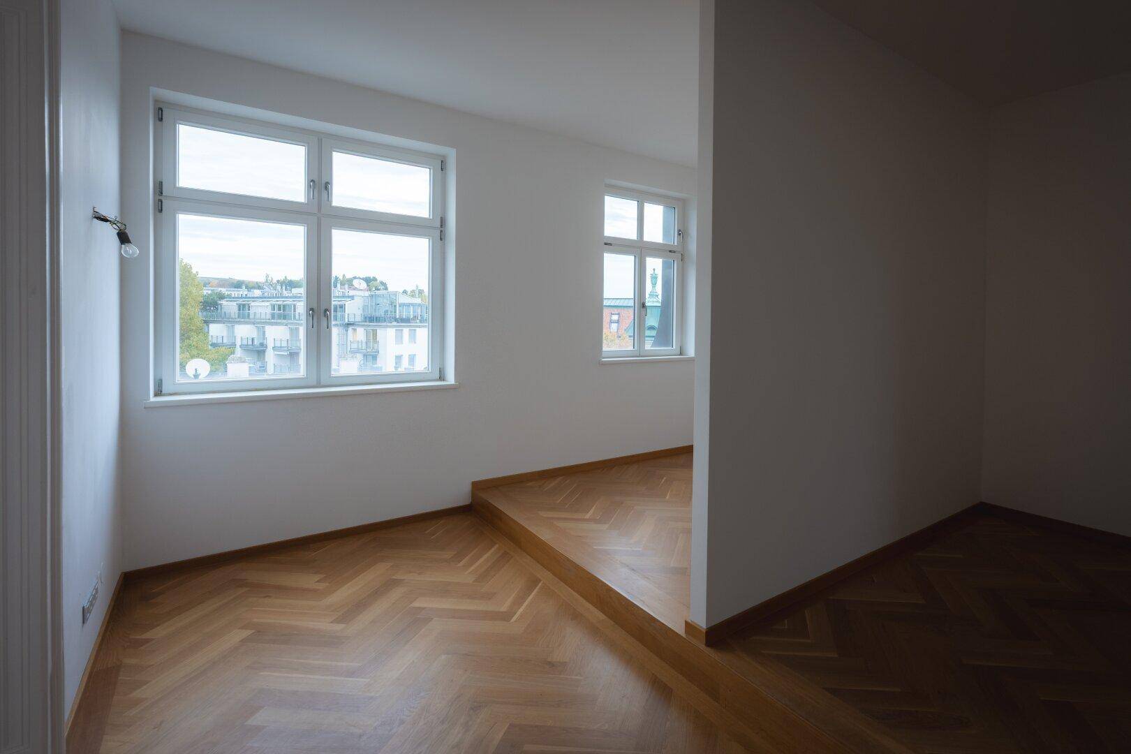 Heller Flurbereich mit Fischgrätparkett und Fenstern, die Tageslicht hereinlassen.