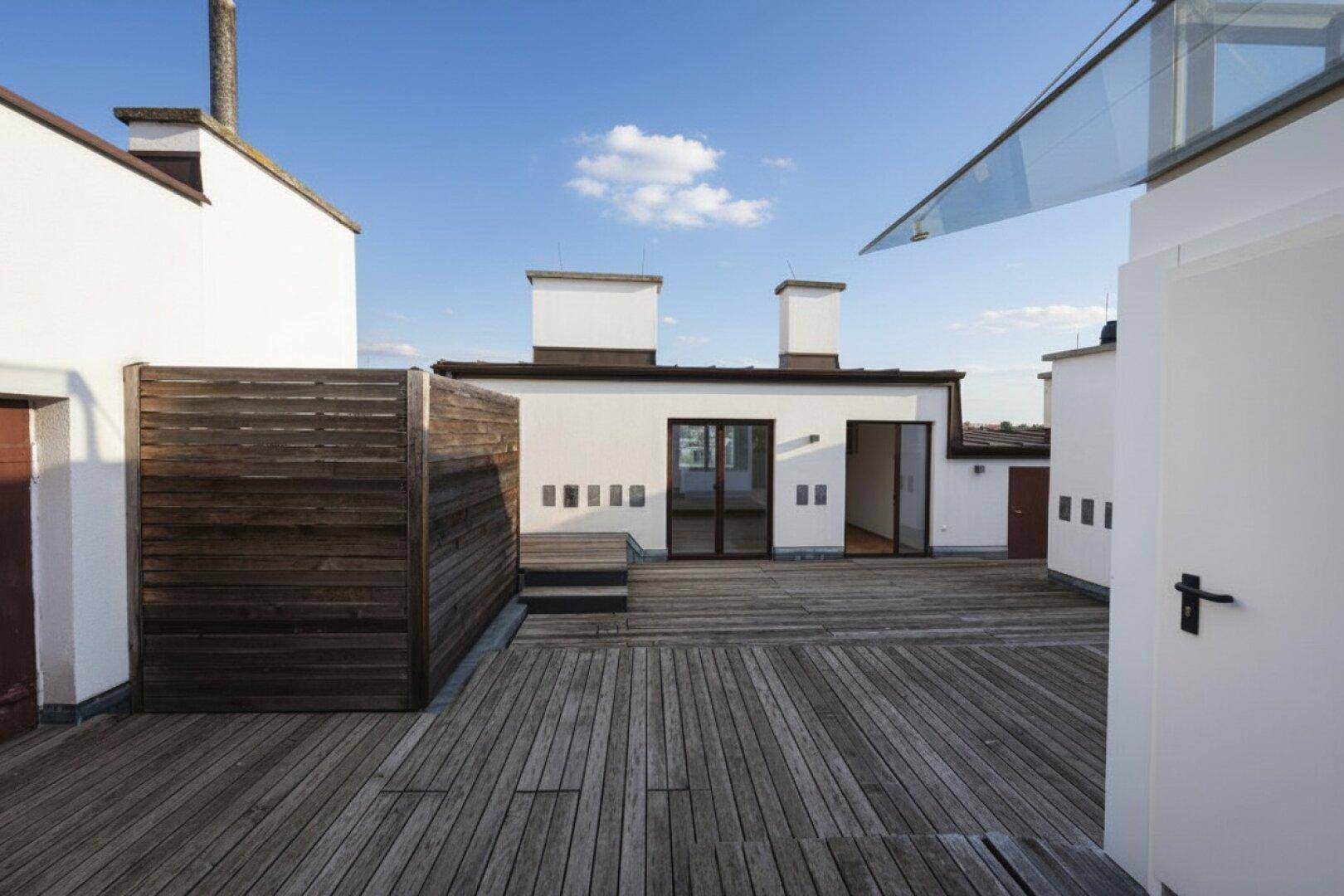 Weitläufige Dachterrasse mit Holzboden und Zugang zu Innenräumen, ideal für Entspannung.