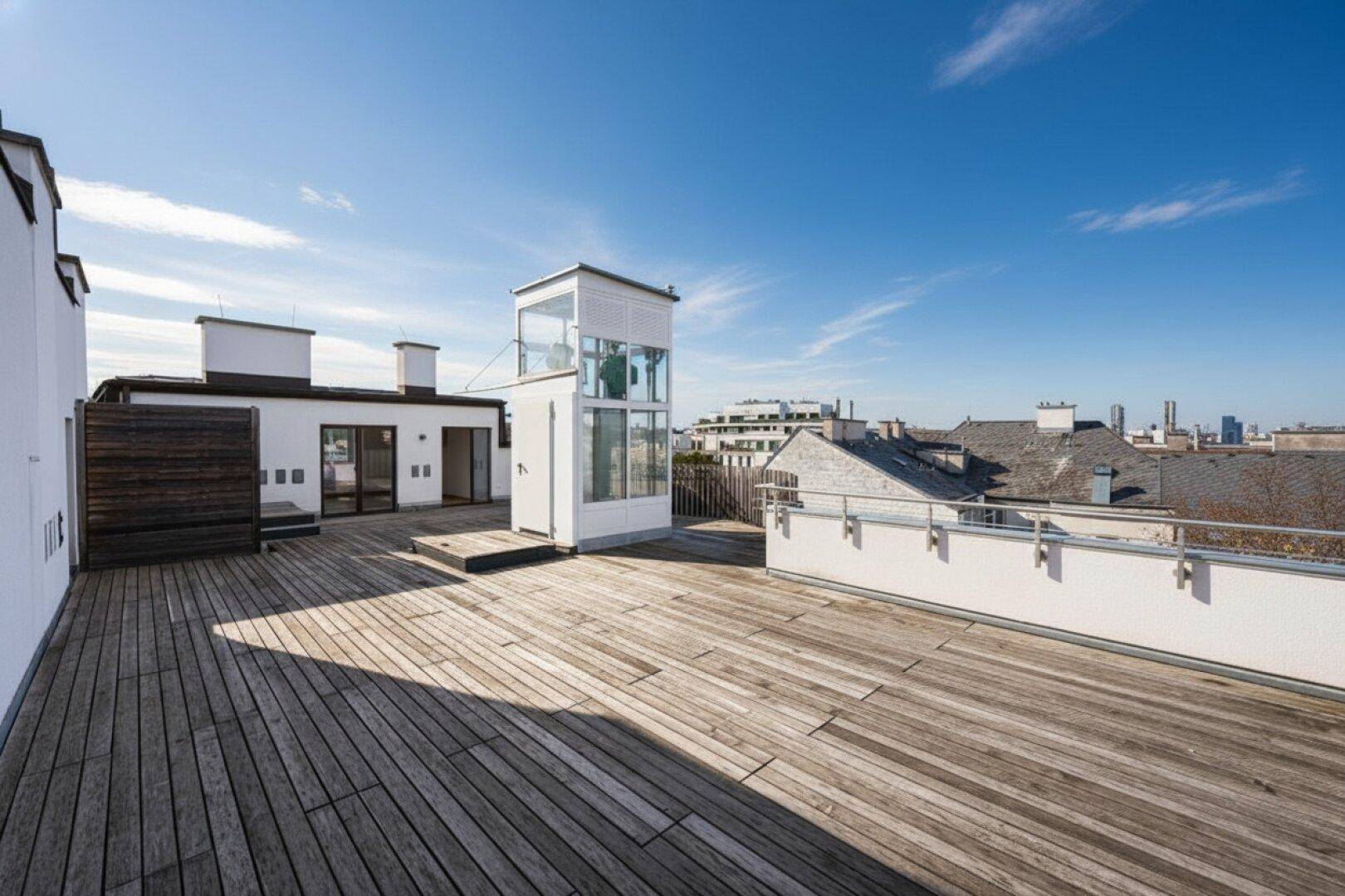Große Dachterrasse mit Holzboden, gläsernem Aufzug und weitem Blick über die Stadt.