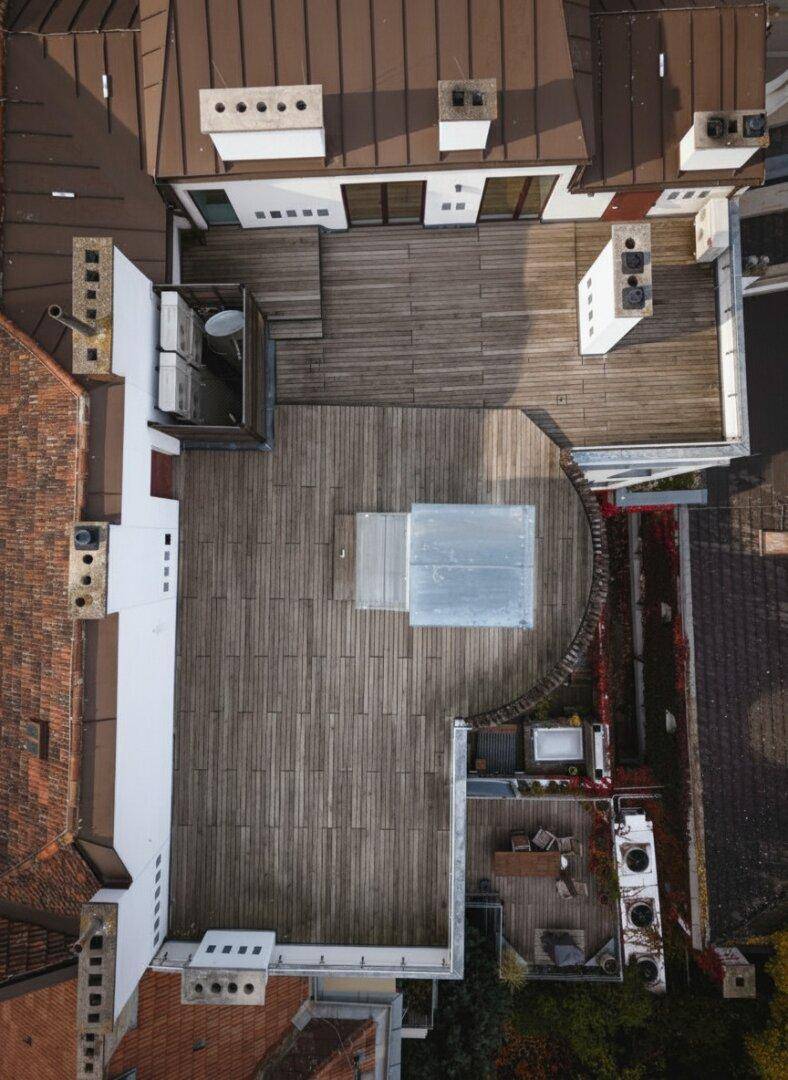 Vogelperspektive auf die große Dachterrasse mit Holzboden und einem gläsernen Aufzug.