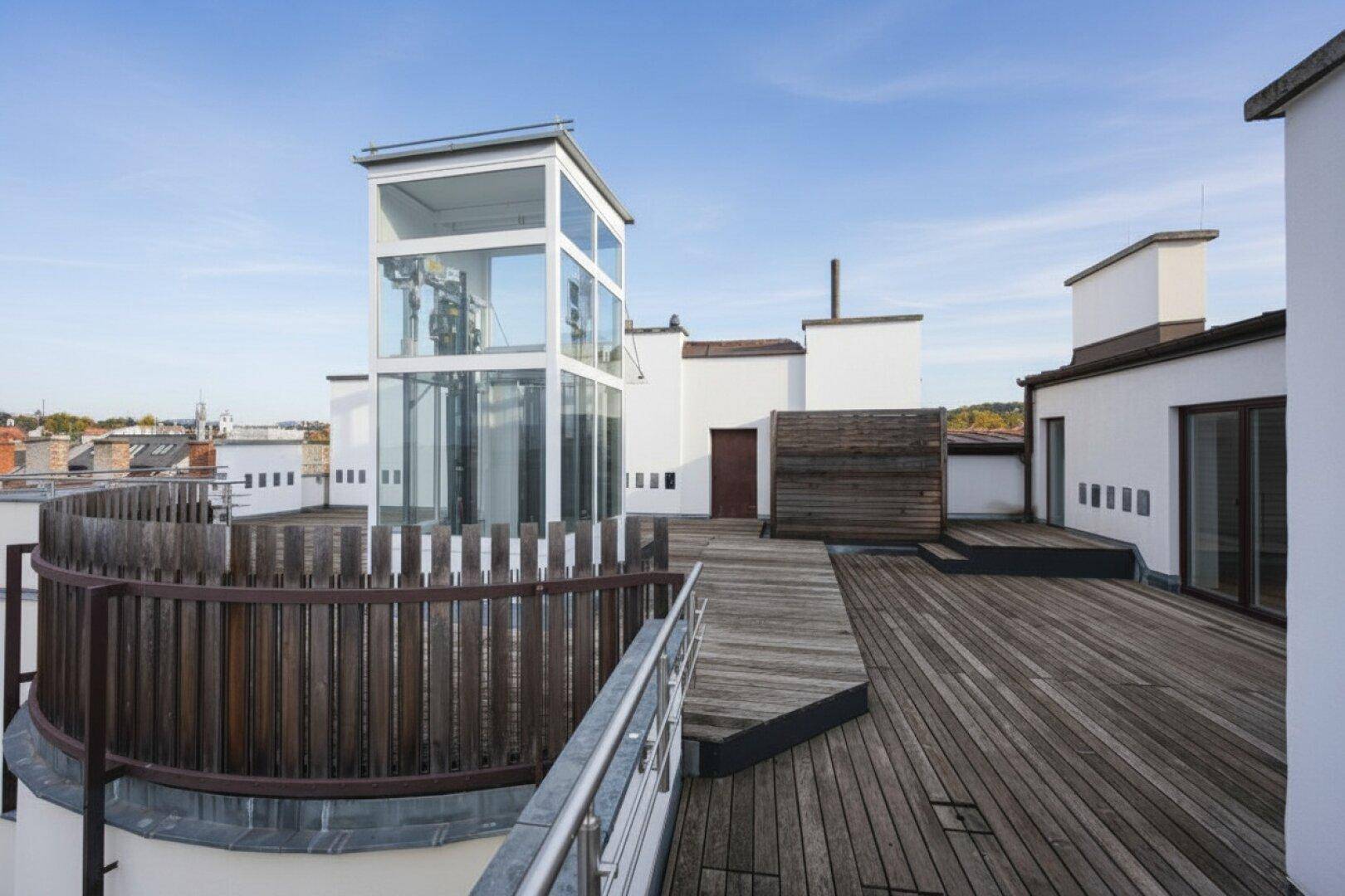 Dachterrasse mit Holzboden, moderner Umzäunung und einem gläsernen Aufzug.