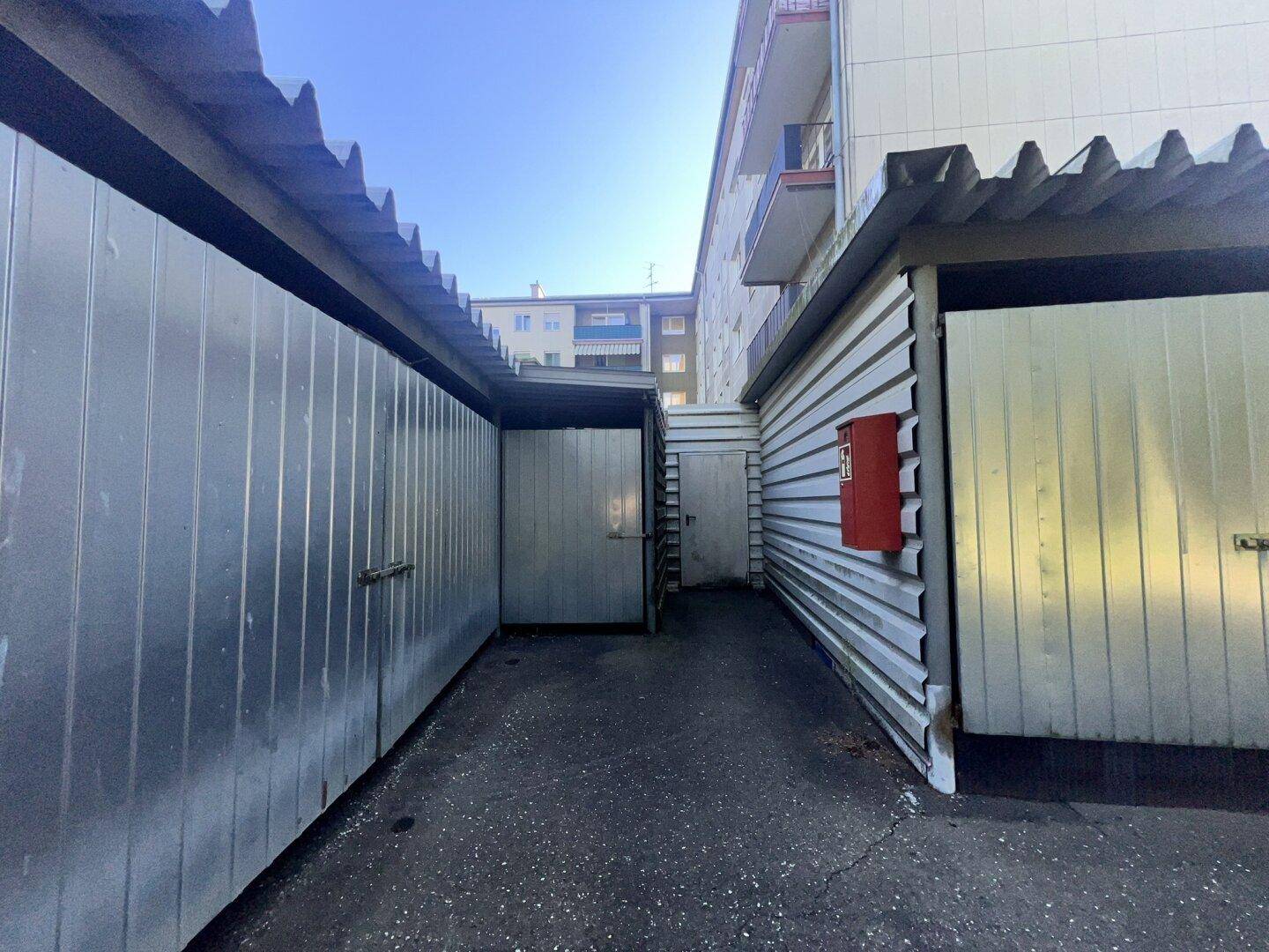 Reihe von Garagenboxen aus Metall mit Wellblechdach und rotem Briefkasten.