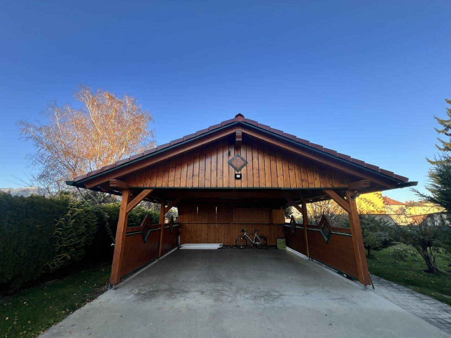 Überdachter Carport aus Holz mit Ziegeldach und Platz für Fahrzeuge und Fahrräder.
