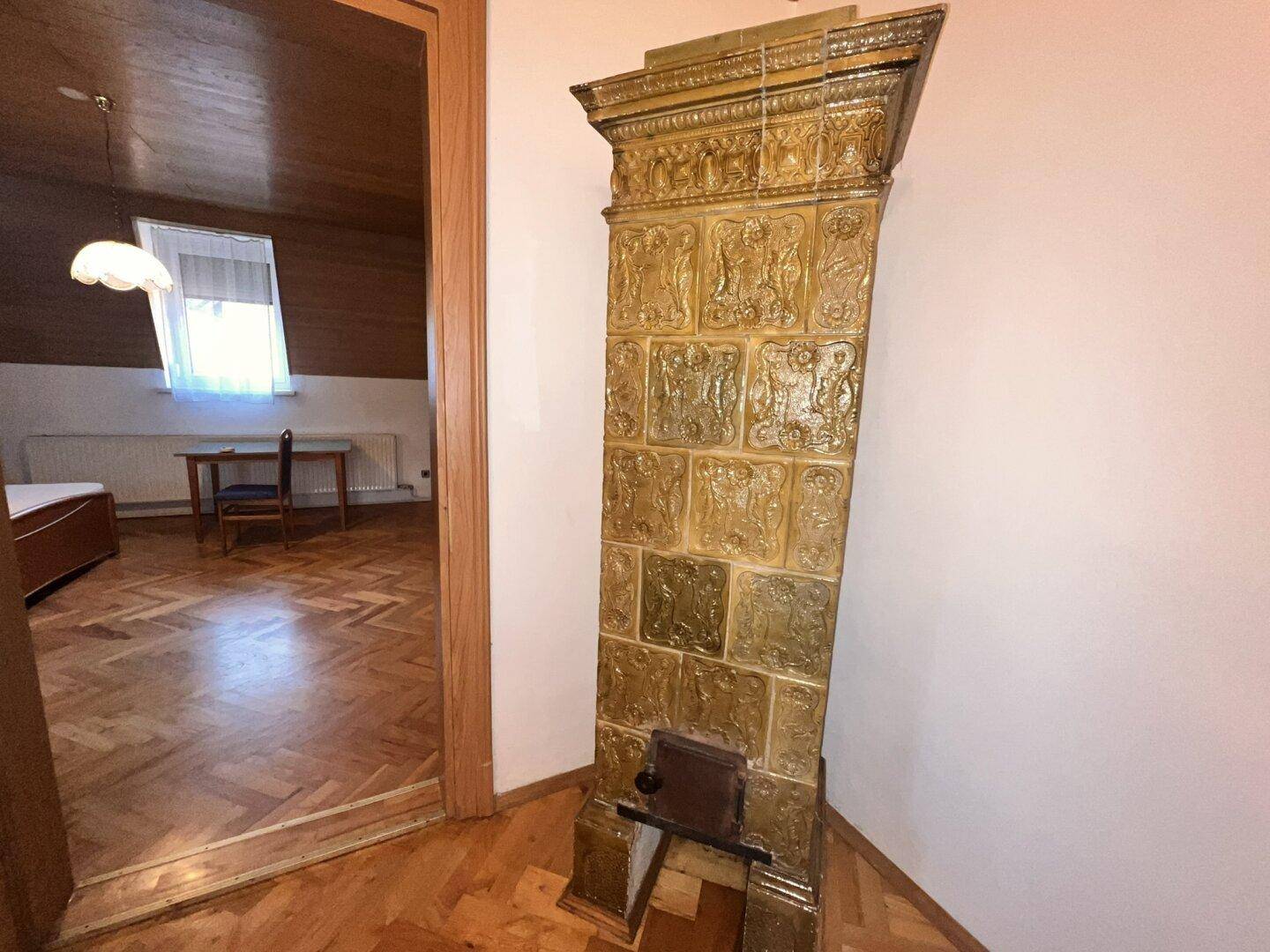 Flur mit traditionellem Kachelofen und Parkettboden, der zu weiteren Räumen führt.