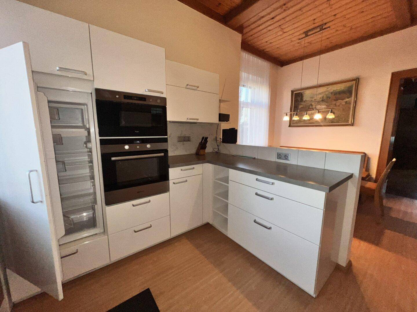 Moderne Einbauküche mit weißen Fronten, integrierten Geräten und Holzdecke.