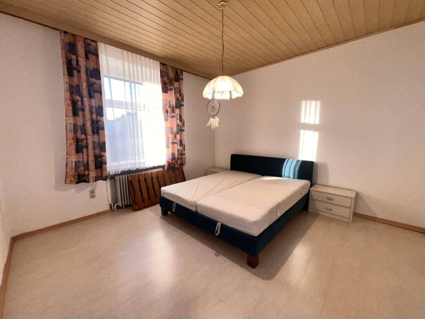 Helles Schlafzimmer mit Doppelbett, Holzboden und Fenster mit Blick ins Grüne.