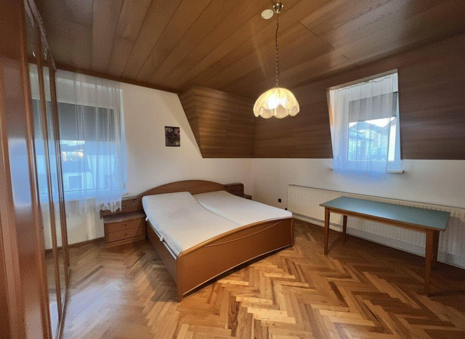 Schlafzimmer mit Holzboden, Doppelbett und zwei Fenstern für gute Belichtung.