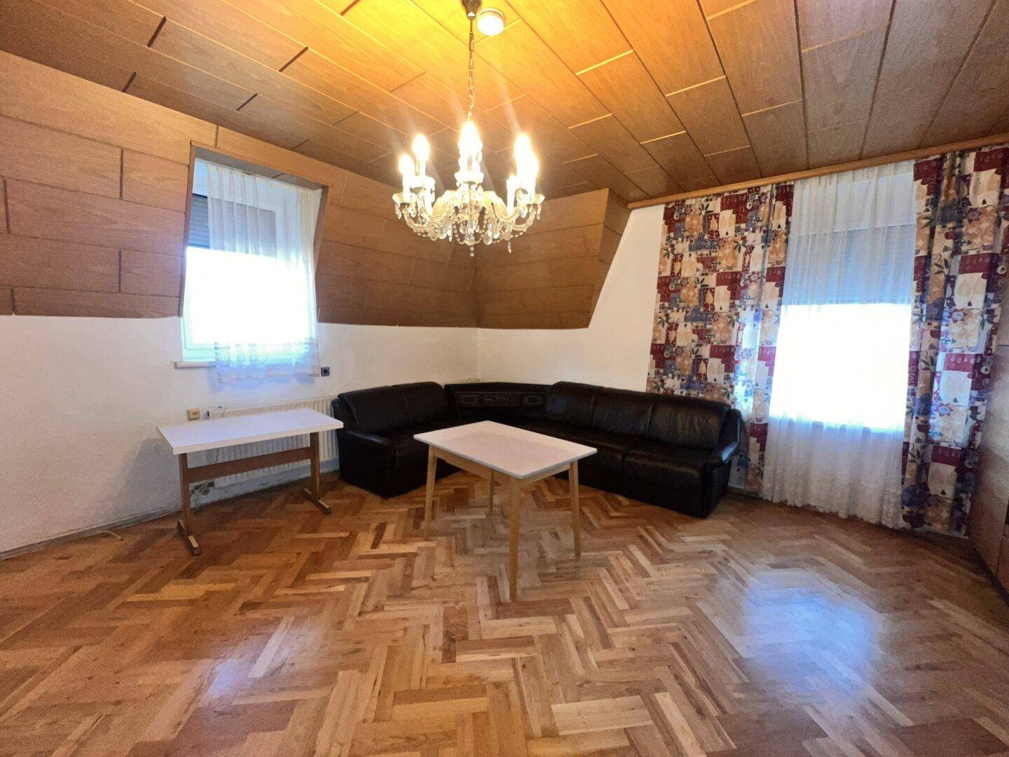 Gemütliches Wohnzimmer mit Parkettboden, Ledersofa und Holzdecke unter einem Kronleuchter.