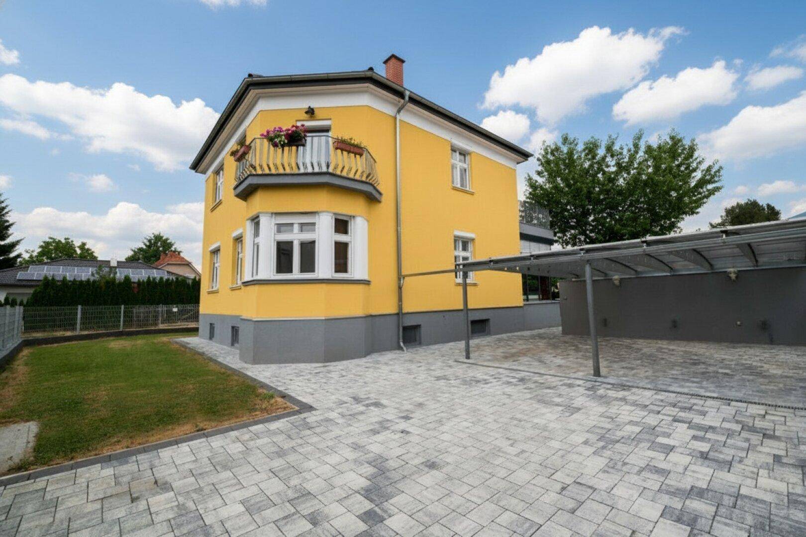 Gelbes Wohnhaus mit gepflasterter Einfahrt und überdachtem Carport.