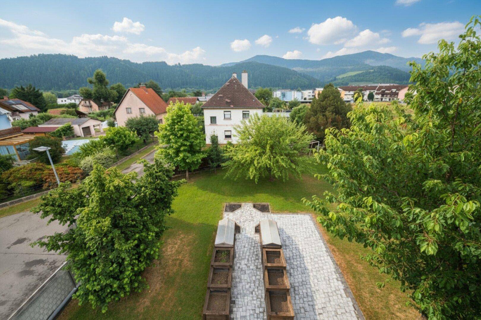 Vogelperspektive des Gartens mit Hochbeeten, Rasenflächen und umliegender Landschaft.