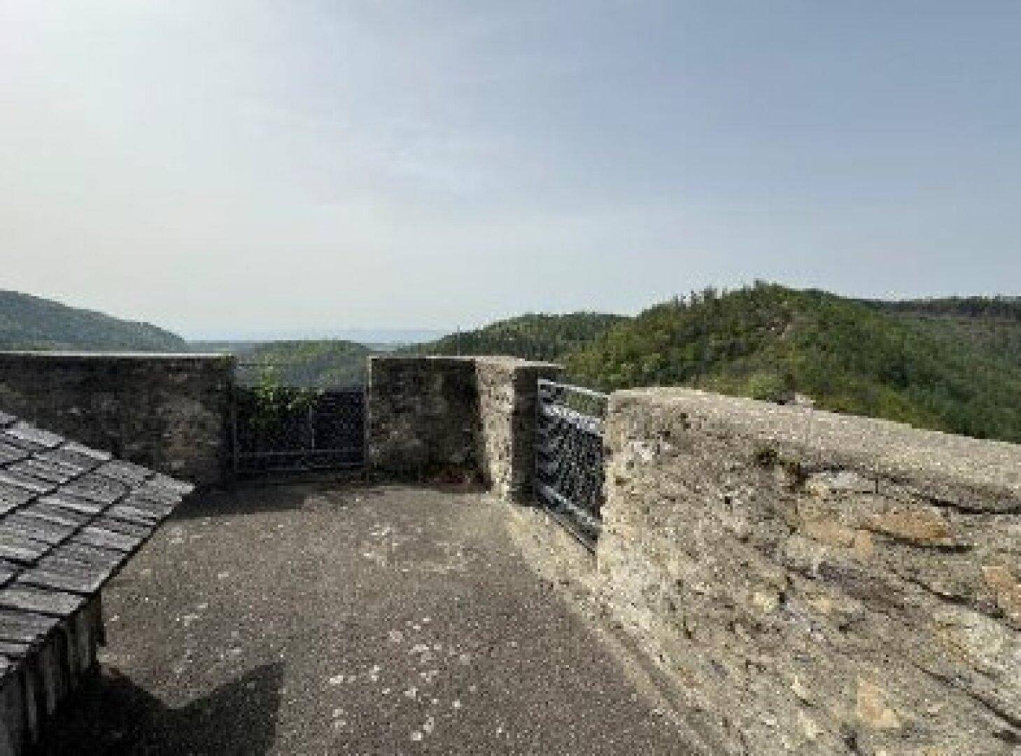 Eine steinerne Terrasse innerhalb der Burgmauern mit Blick auf die weite, grüne Landschaft.