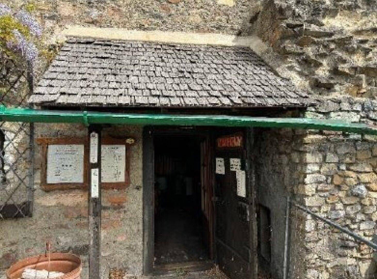Eingangsbereich eines Gebäudes innerhalb der Burgruine mit Holzdach und Steinmauern.