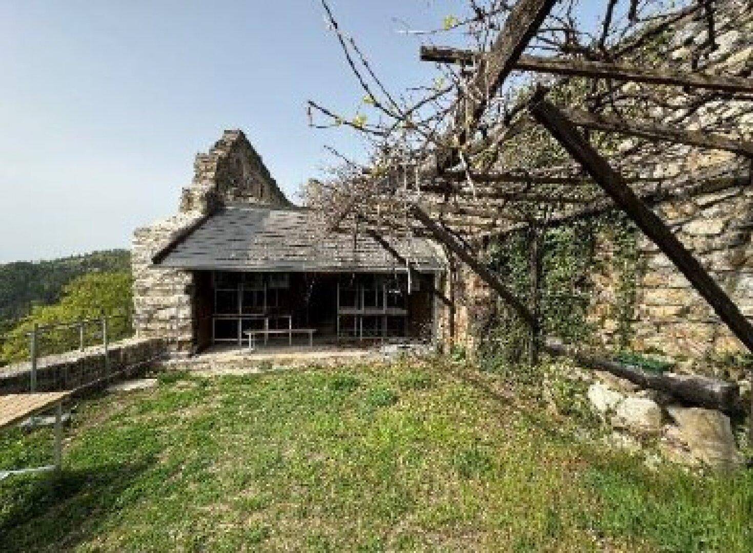 Ein begrünter Innenhof einer Burgruine mit einer überdachten Struktur und alten Steinmauern.