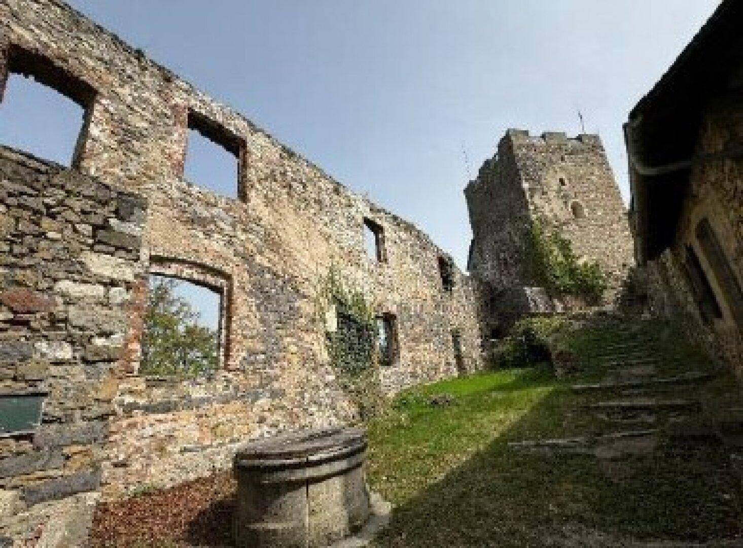 Innenhof einer Burgruine mit hohen Steinmauern, Fensteröffnungen und einem alten Brunnen.