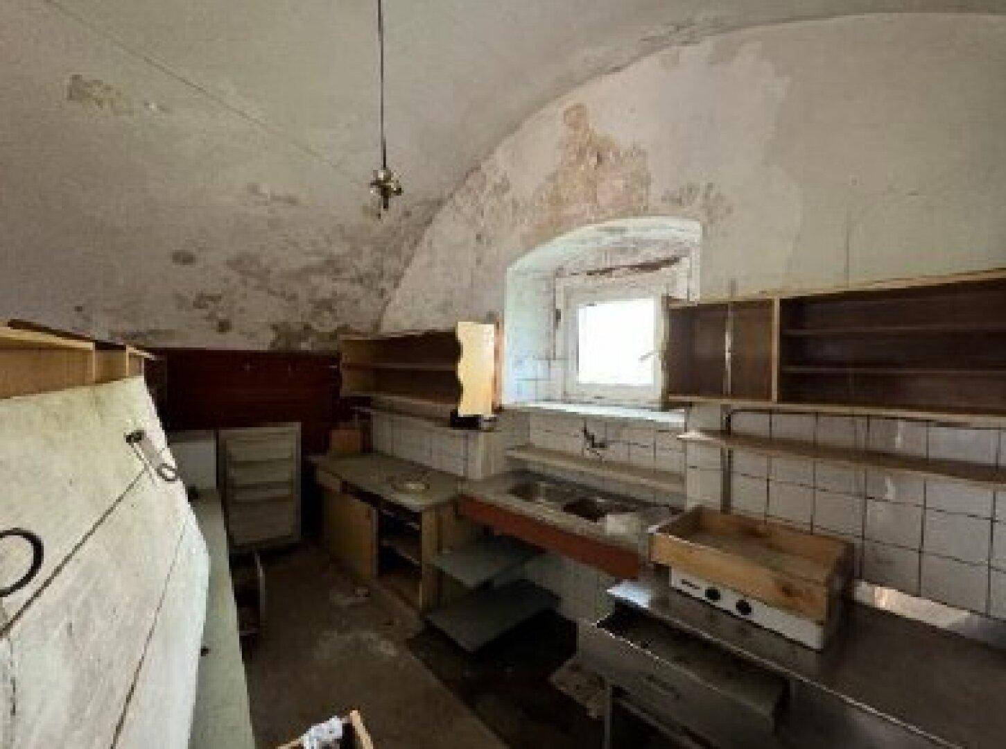 Alte Küche mit gewölbter Decke, einfachen Regalen, Fliesen und einem Fenster.