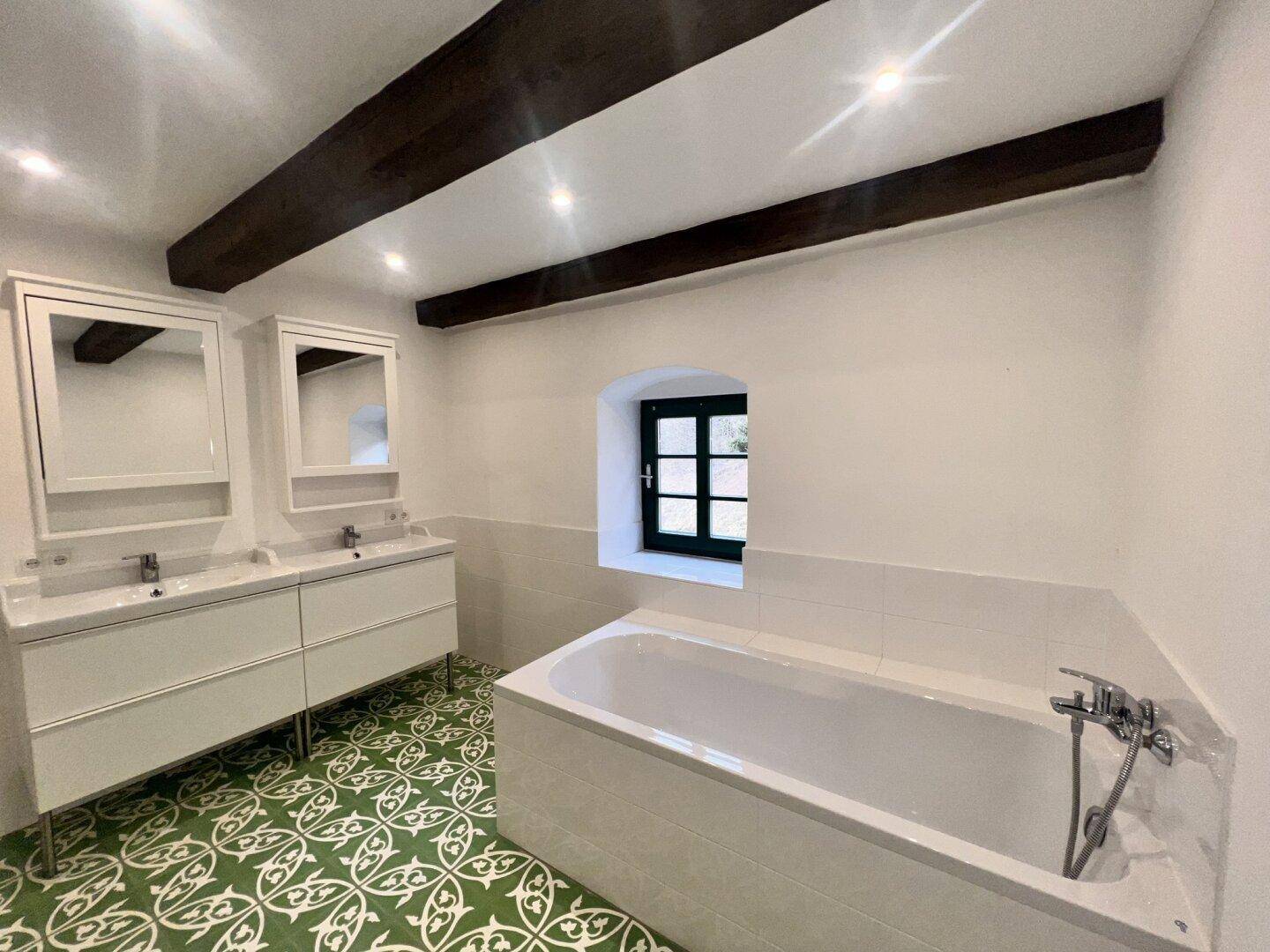 Modernisiertes Badezimmer mit Doppelwaschbecken, Badewanne und gemusterten grünen Bodenfliesen.