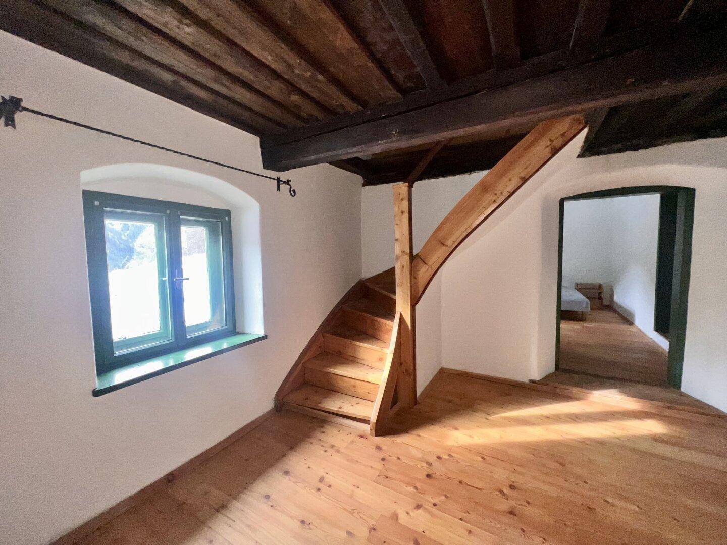 Holztreppe führt in den oberen Bereich, umgeben von Holzdielenboden und sichtbaren Balken.