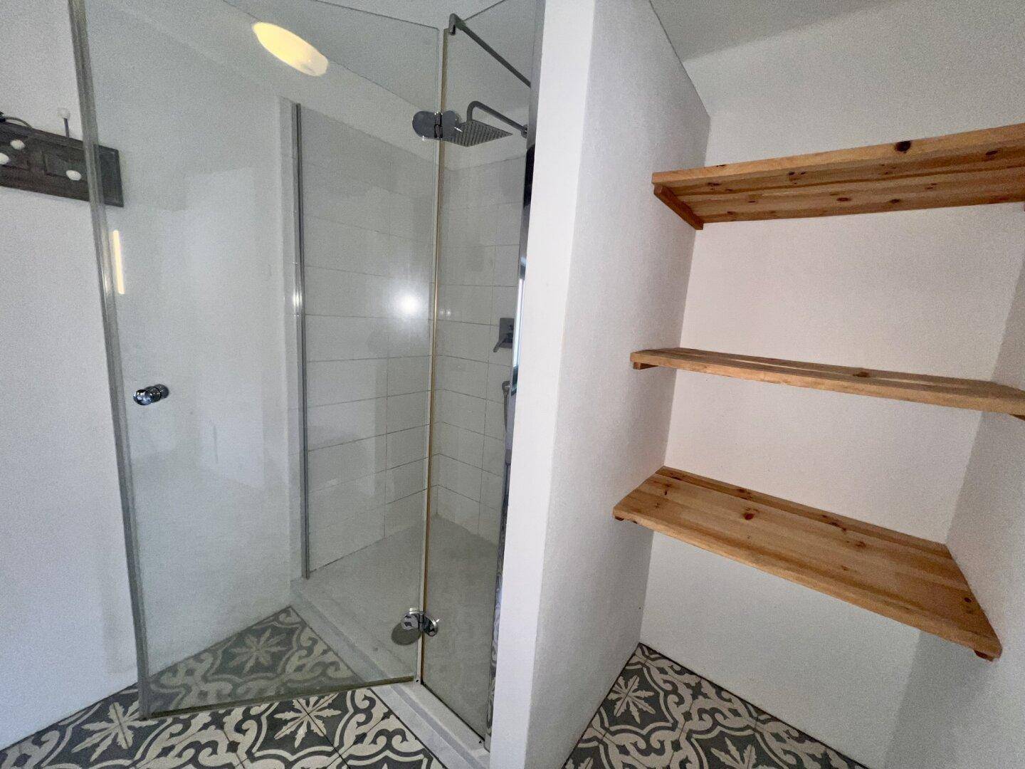 Duschbereich mit Glasabtrennung, modernen Fliesen und Holzregalen im Badezimmer.