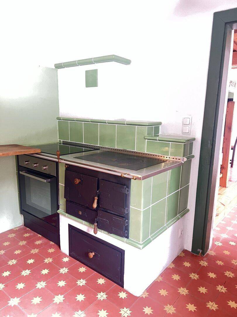 Detailansicht des traditionellen grünen Kachelofens mit integriertem Backofen in der Küche.