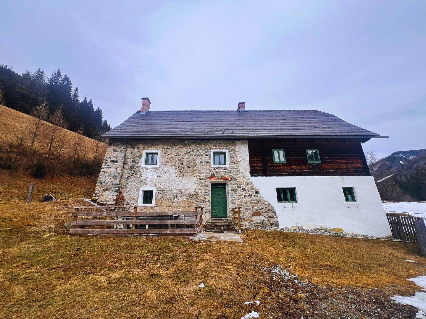 Historisches Bauernhaus mit Steinfassade und Holzelementen in ländlicher Umgebung.