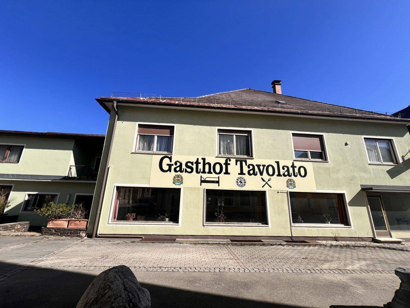 Frontansicht des Gasthofs an einem sonnigen Tag mit großen Fenstern im Erdgeschoss.