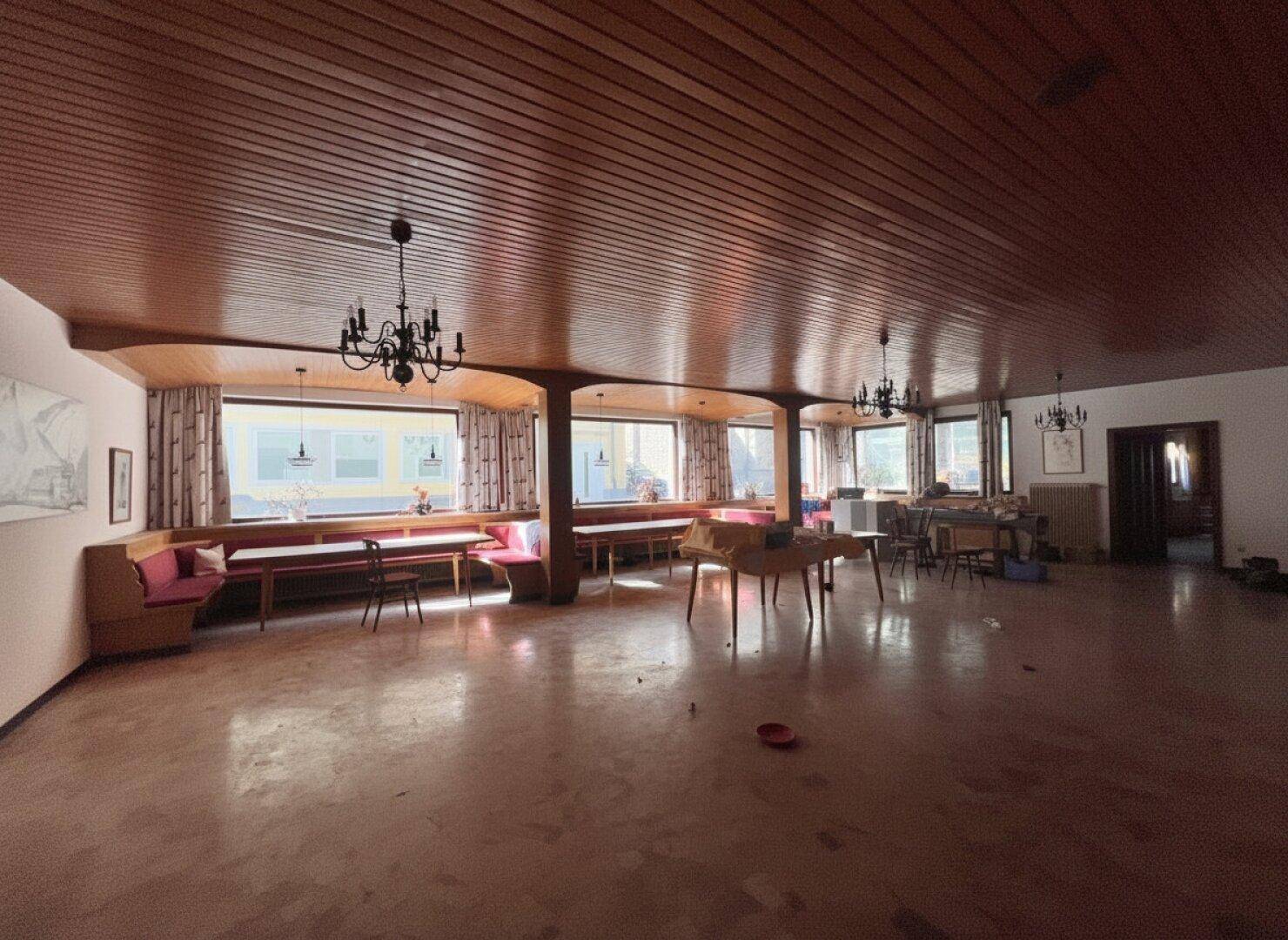 Großer Gastraum mit Holztäfelung an der Decke, langen Sitzbänken und Kronleuchtern.