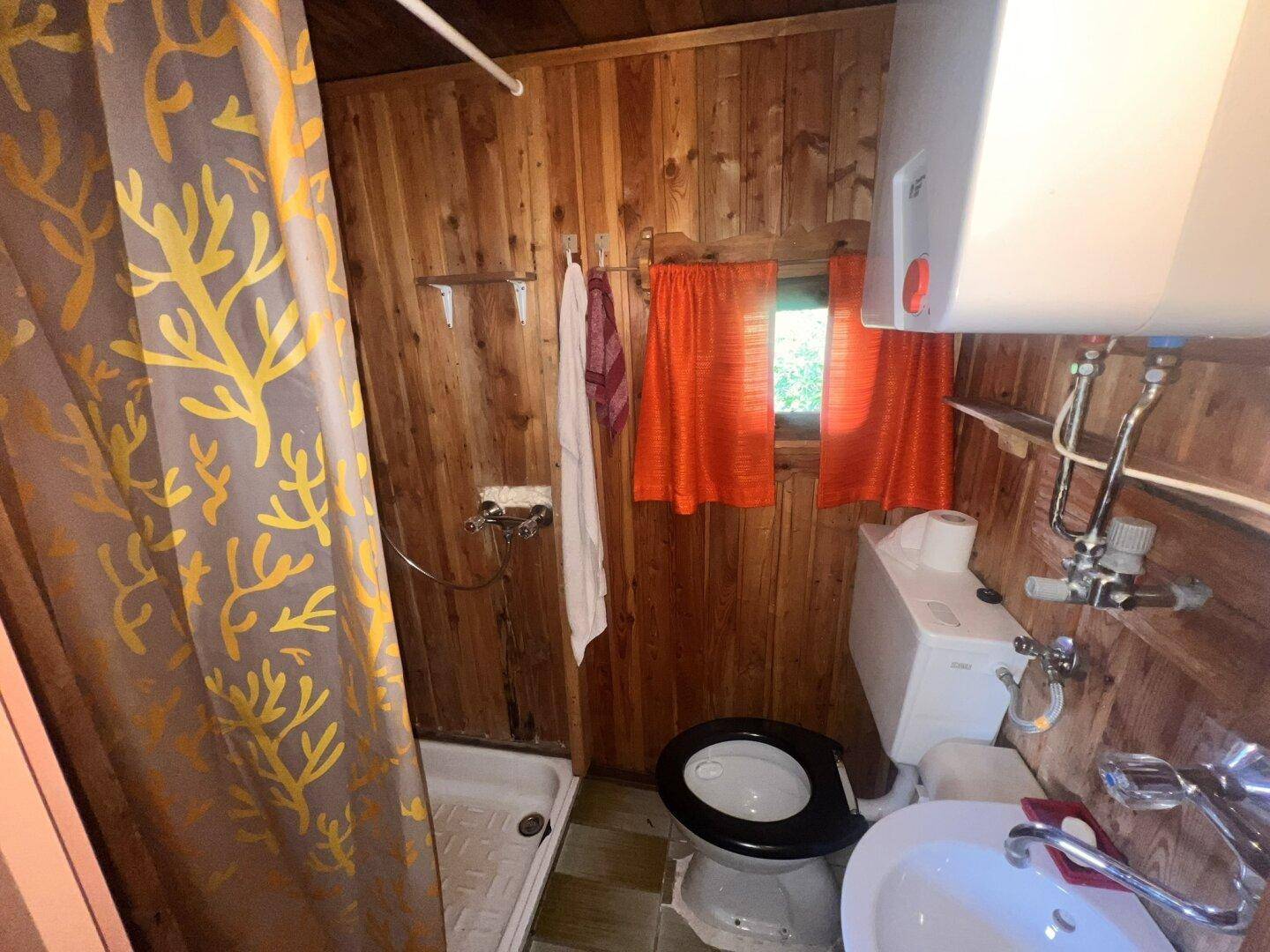 Kleines Badezimmer mit Holztäfelung, Dusche, WC und Waschbecken in rustikalem Stil.