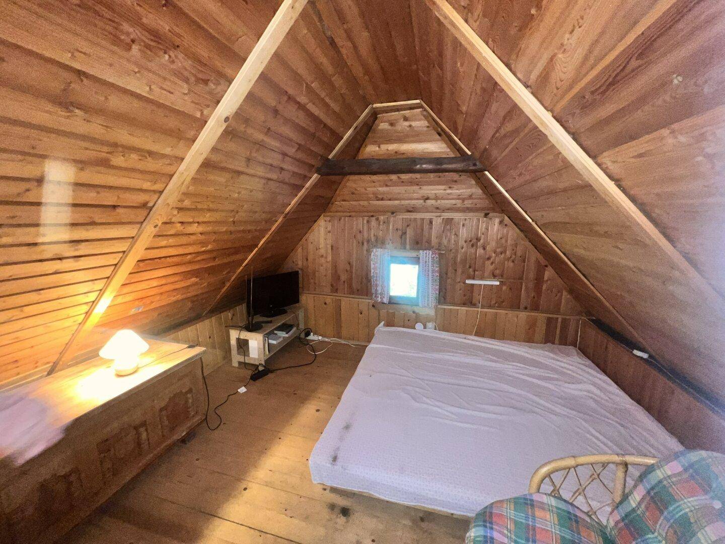 Gemütliches Schlafzimmer im Dachgeschoss mit Holztäfelung, schrägen Wänden und kleinem Fenster.