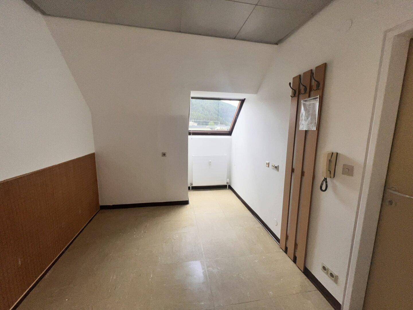 Schlichter Raum mit Dachschräge, Fenster und Holzverkleidung, genutzt als Abstell- oder Waschraum.