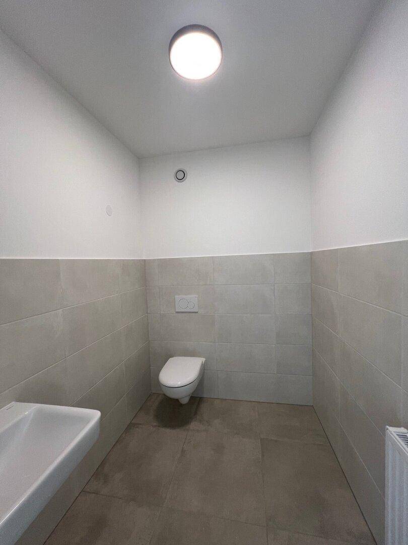 Sauberes WC mit wandhängender Toilette, Einzelwaschbecken und hellen Fliesen.