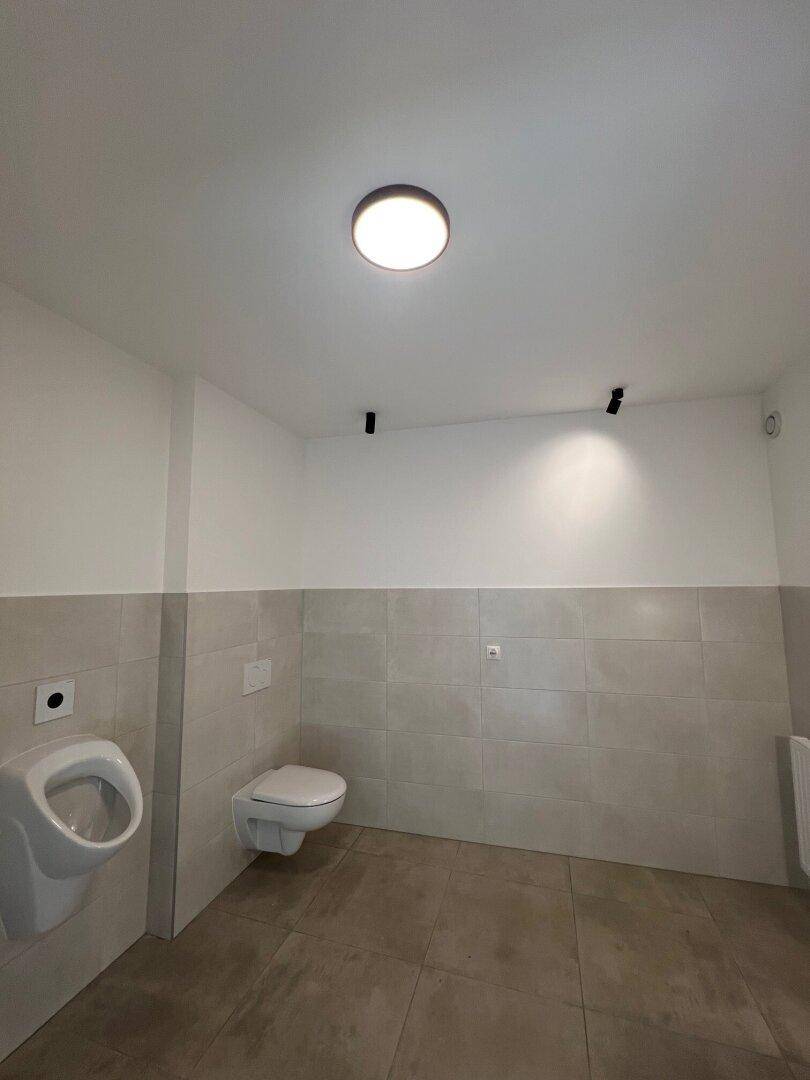 Modern gefliestes WC mit Urinal und wandhängender Toilette in neutralen Farben.