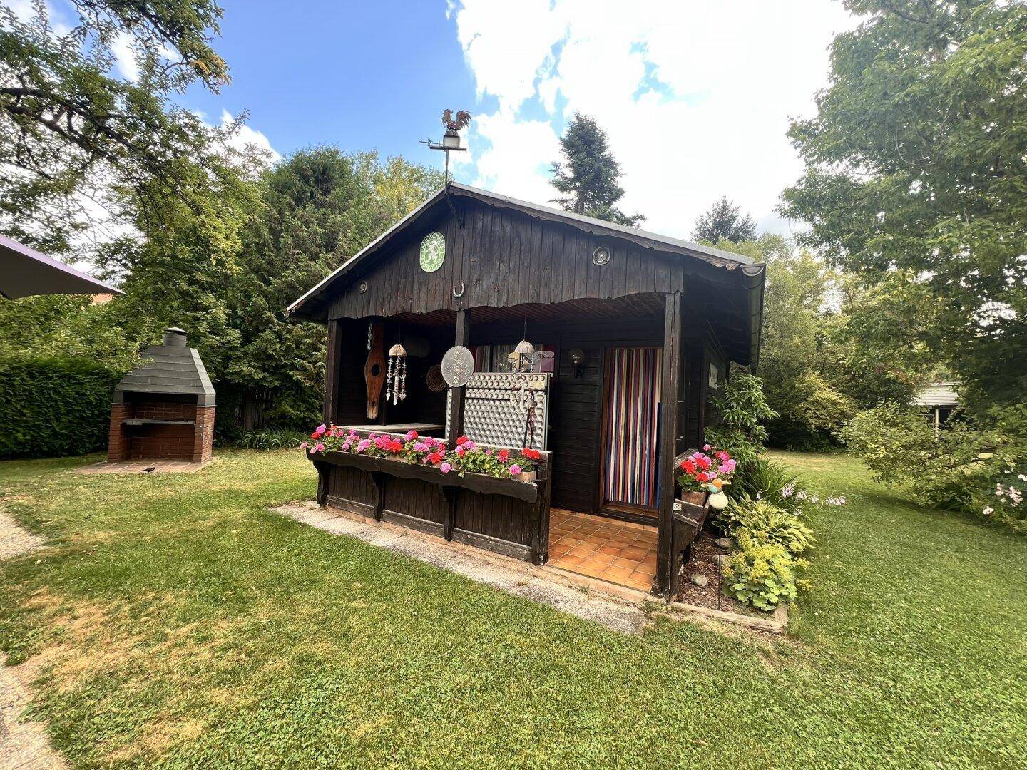 Charmantes Gartenhaus mit Blumen und Grillplatz im weitläufigen grünen Garten.