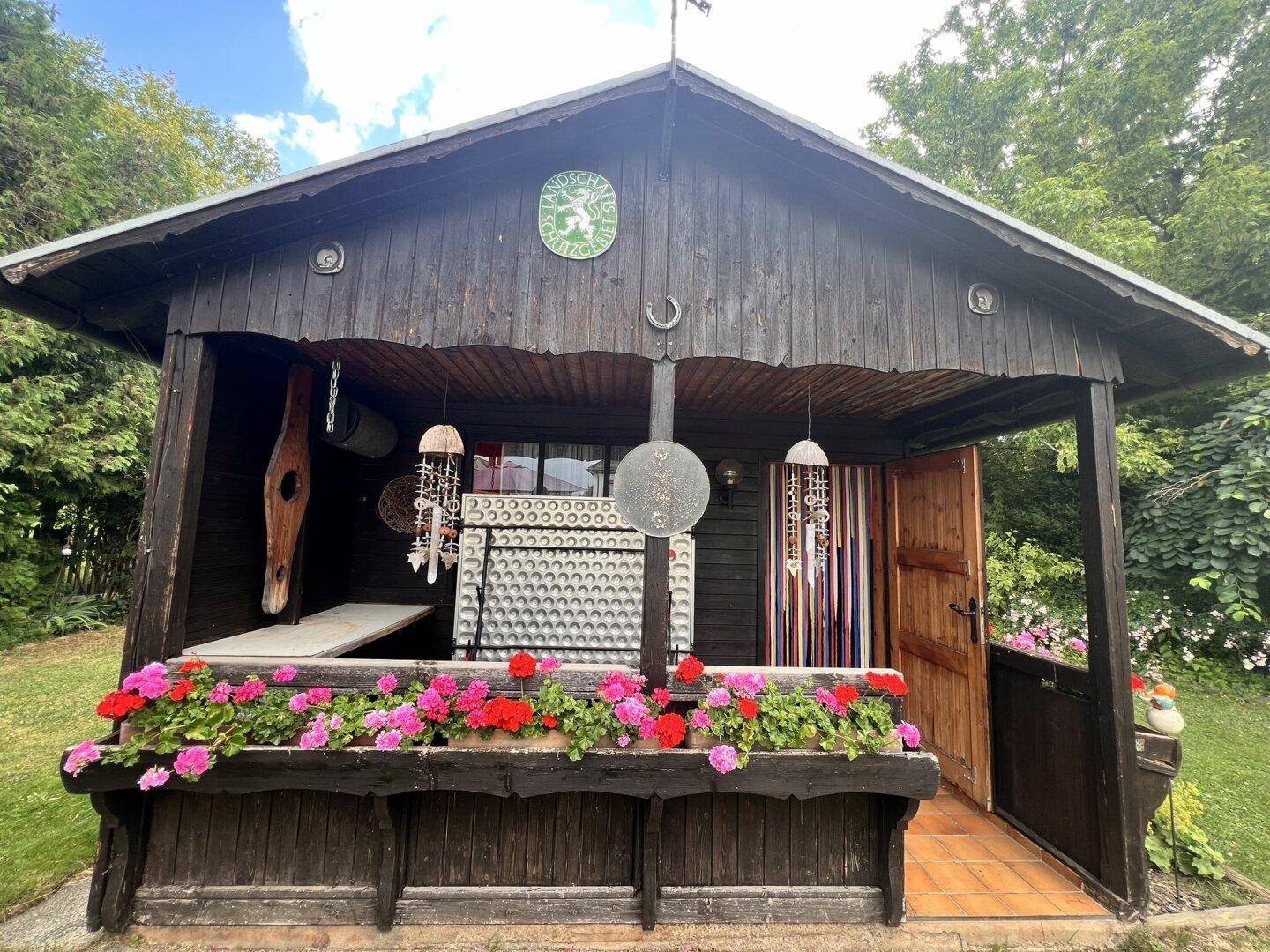 Rustikales Gartenhaus aus Holz mit Blumenkästen und traditioneller Dekoration.