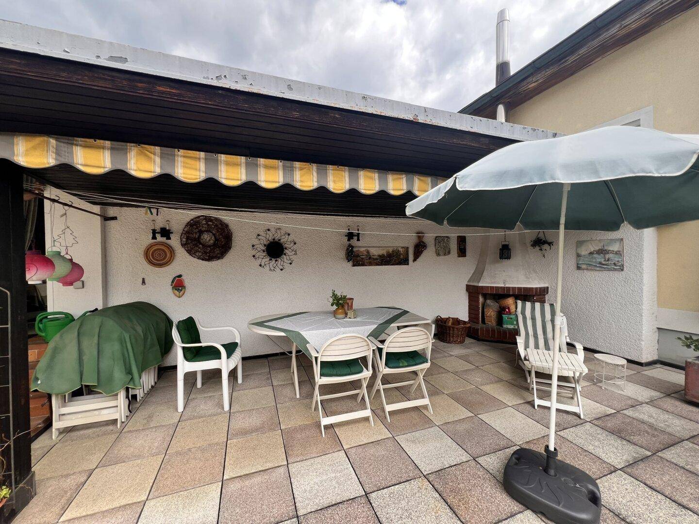 Überdachte Terrasse mit Essbereich, Kamin und Markise für gemütliche Stunden im Freien.