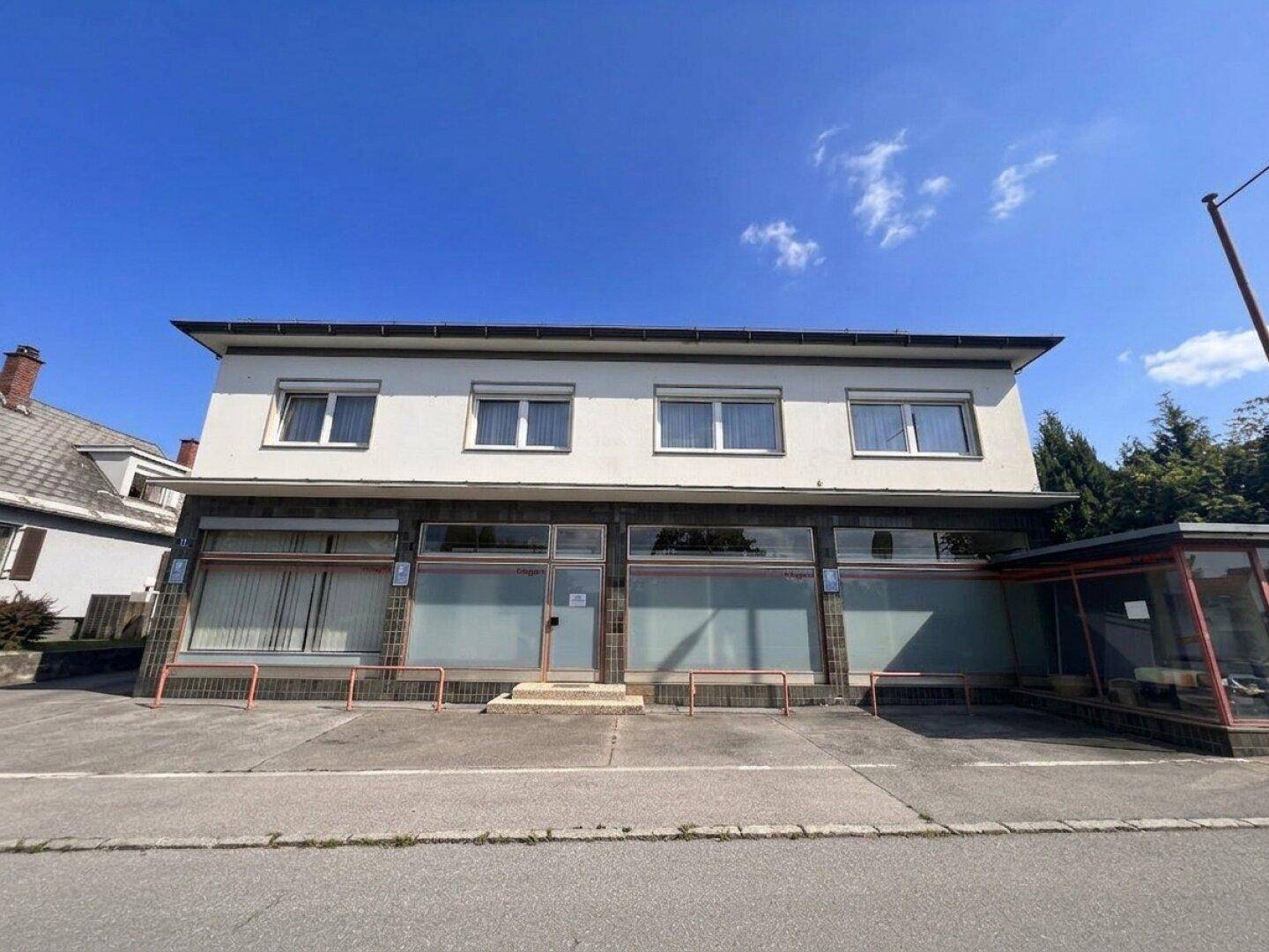 Fassade eines Geschäftsgebäudes mit großen Schaufenstern und Parkplätzen davor.