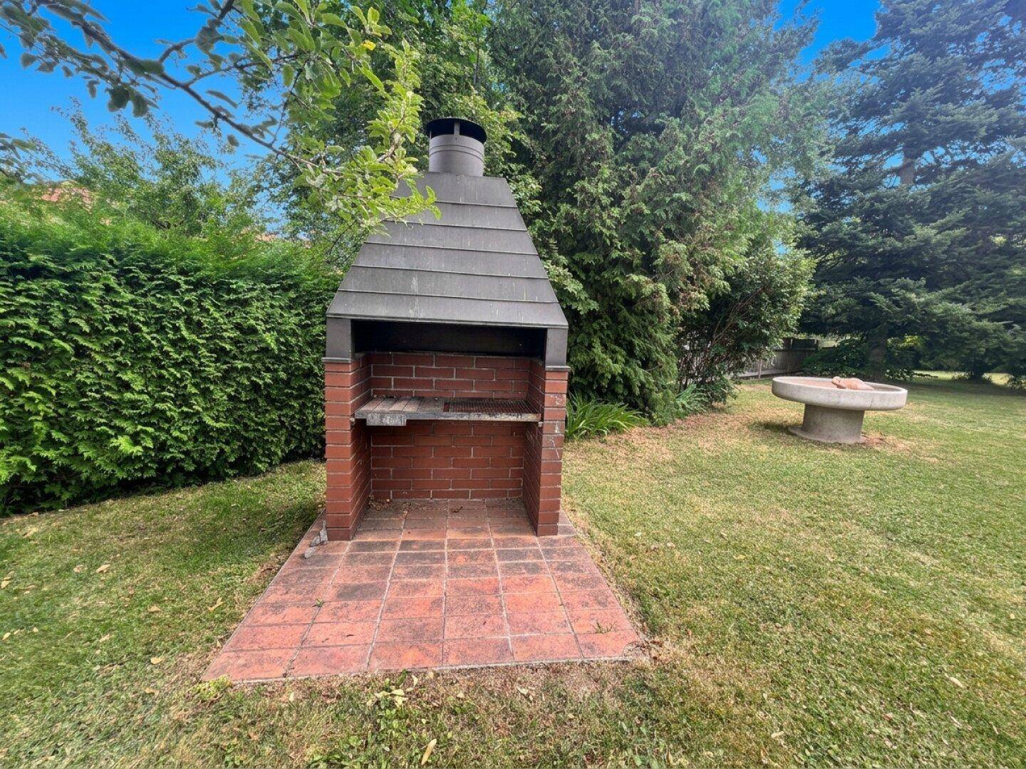 Gemauerter Grillplatz mit Ziegeln und Steinfliesen im grünen Gartenbereich.