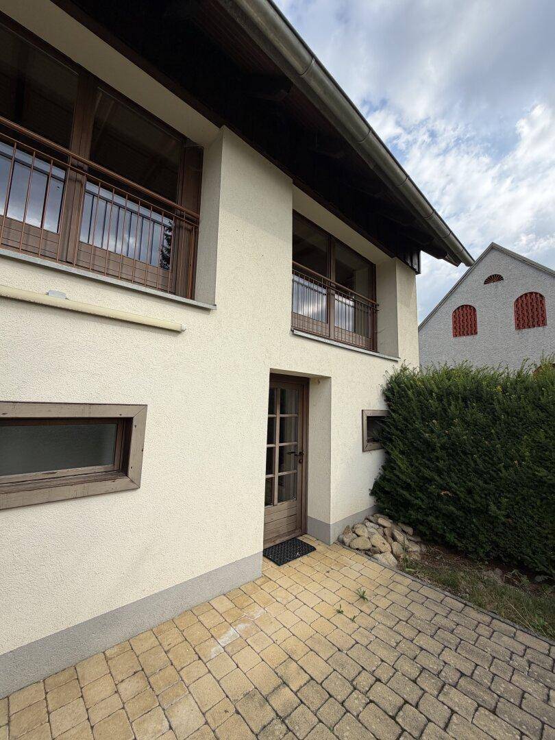 Seitenansicht des Gebäudes mit französischen Balkonen und gepflastertem Zugangsbereich.