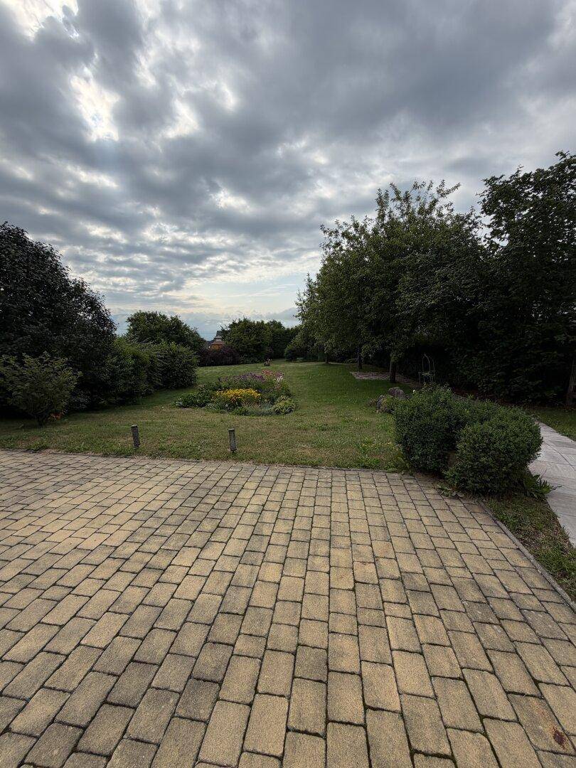 Weitläufiger Gartenbereich mit Rasenfläche, altem Baumbestand und gepflastertem Weg.