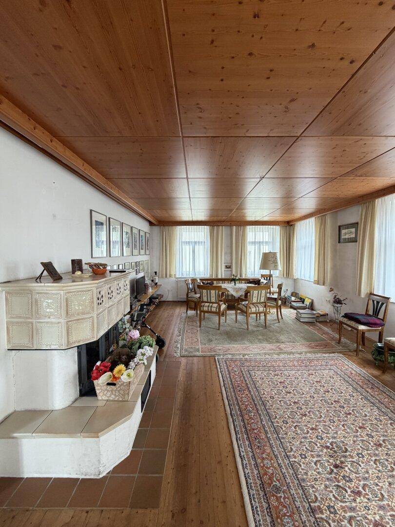 Gemütlicher Wohn-Essbereich mit Holzbalkendecke, Dielenboden und traditionellem Kachelofen.