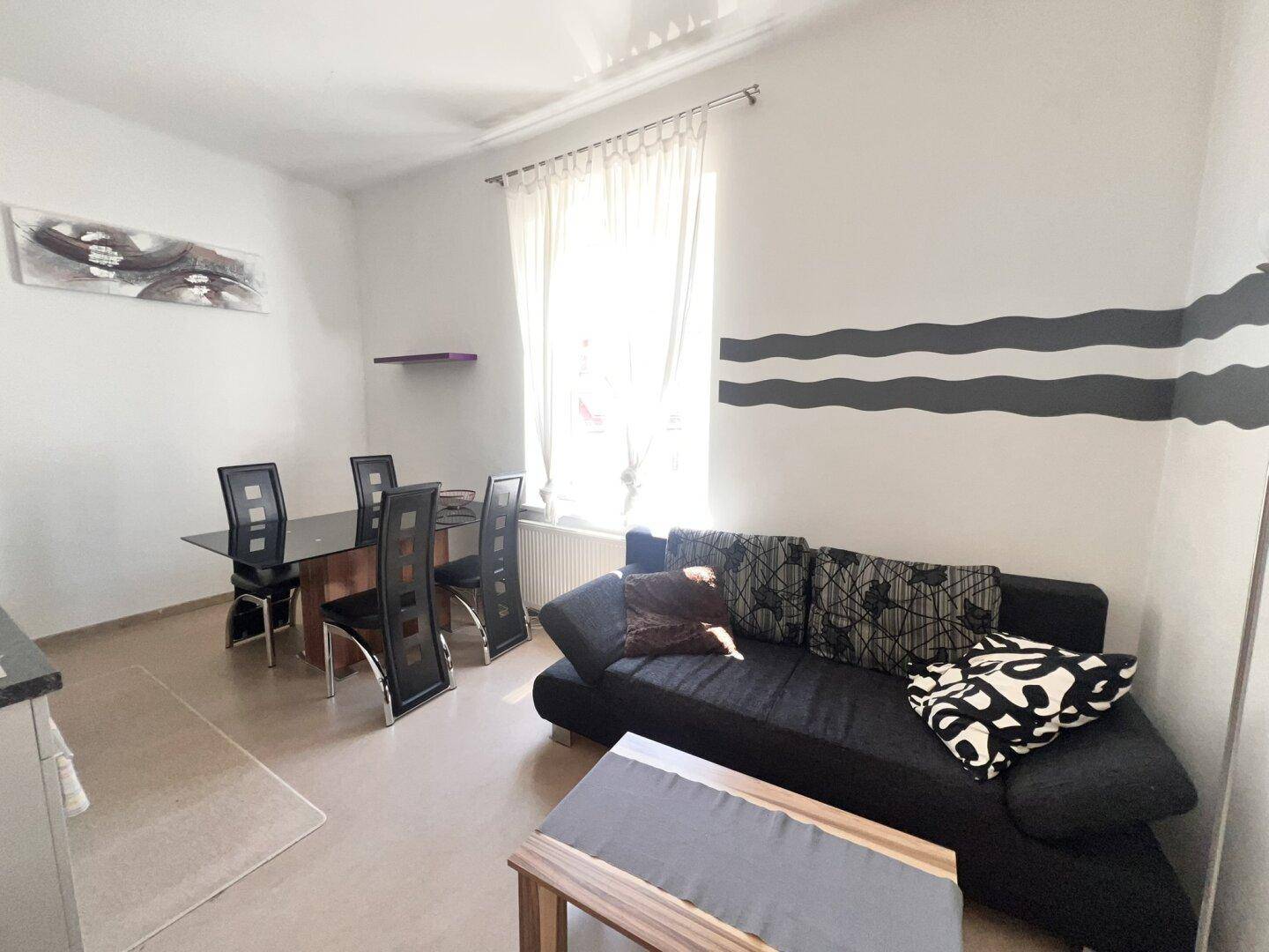 Heller Wohn- und Essbereich mit Sofa, Esstisch und dekorativen Wandstreifen.