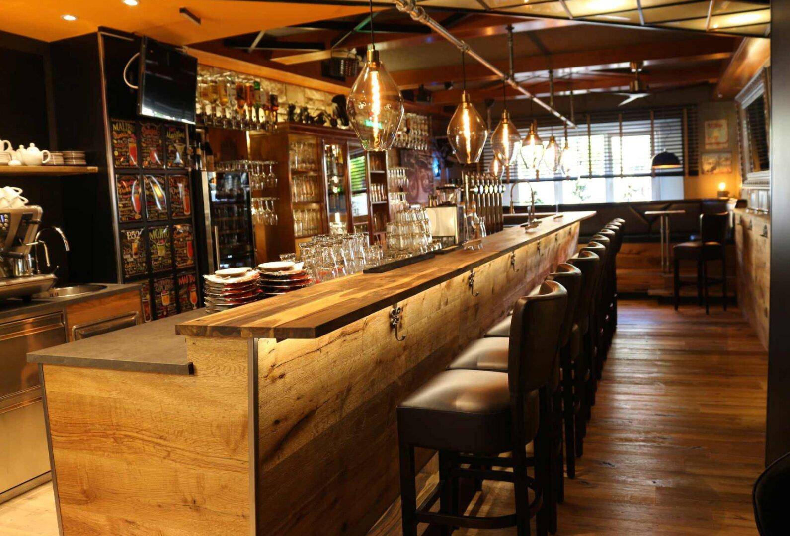 Rustikale Bar mit Holztheke, Barhockern und industriellen Pendelleuchten, gut beleuchtet.