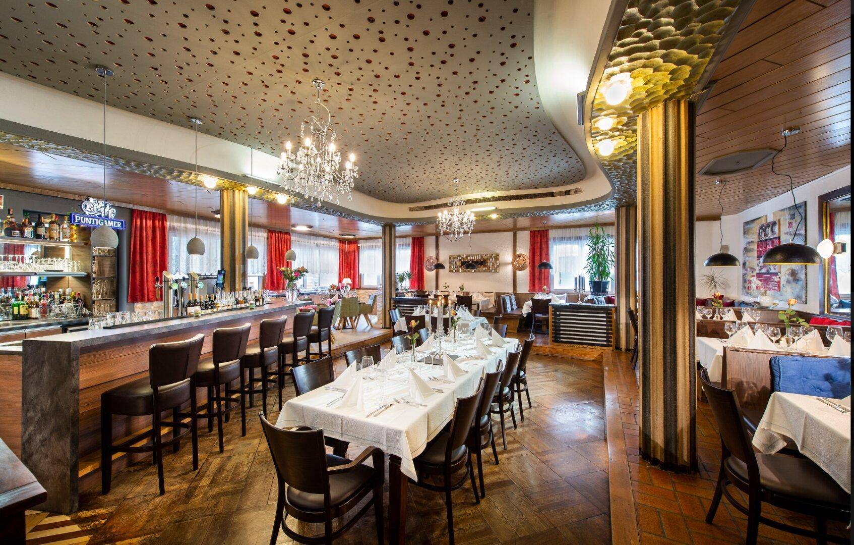 Großer, eleganter Speisesaal mit einer langen Bar, Kronleuchtern und vielen gedeckten Tischen, mit Holzböden.