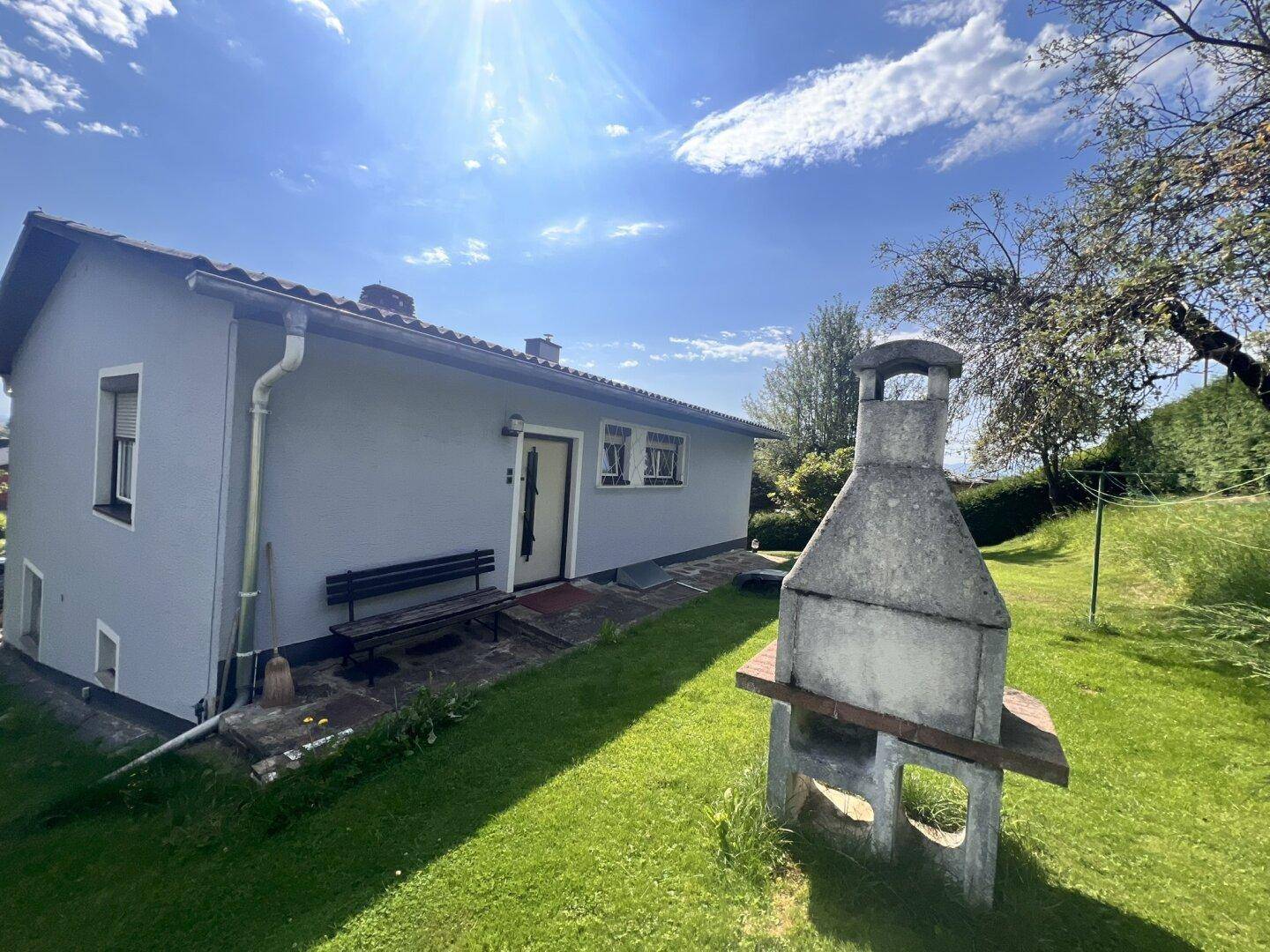 Sonniger Garten mit großzügiger Rasenfläche und einem gemauerten Grill, ideal für Sommerabende.