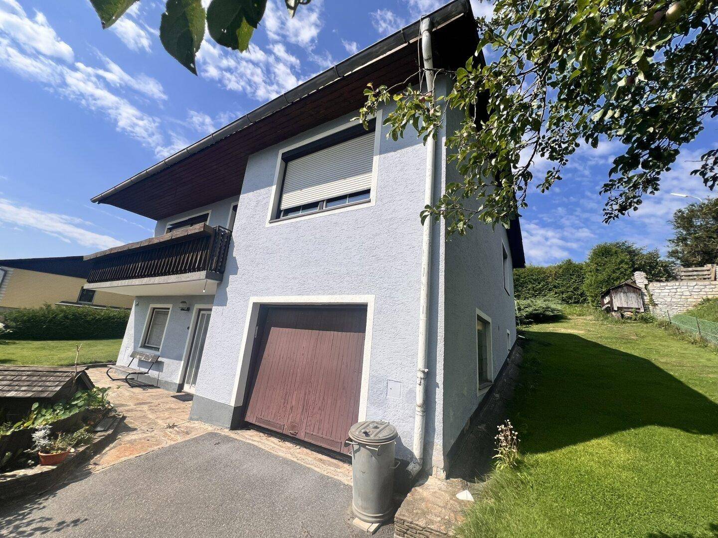Hausfassade mit integrierter Garage, Balkon und gepflegter Auffahrt unter blauem Sommerhimmel.