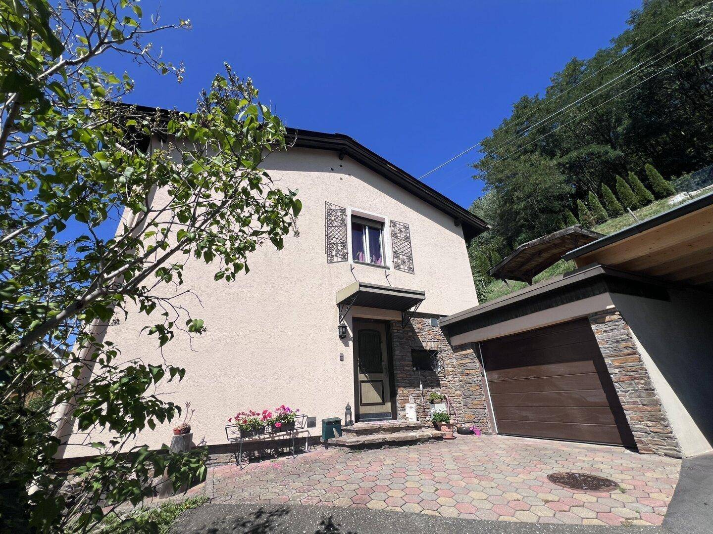 Vorderansicht des Hauses mit Eingangsbereich, Garage und gepflasterter Auffahrt unter blauem Himmel.