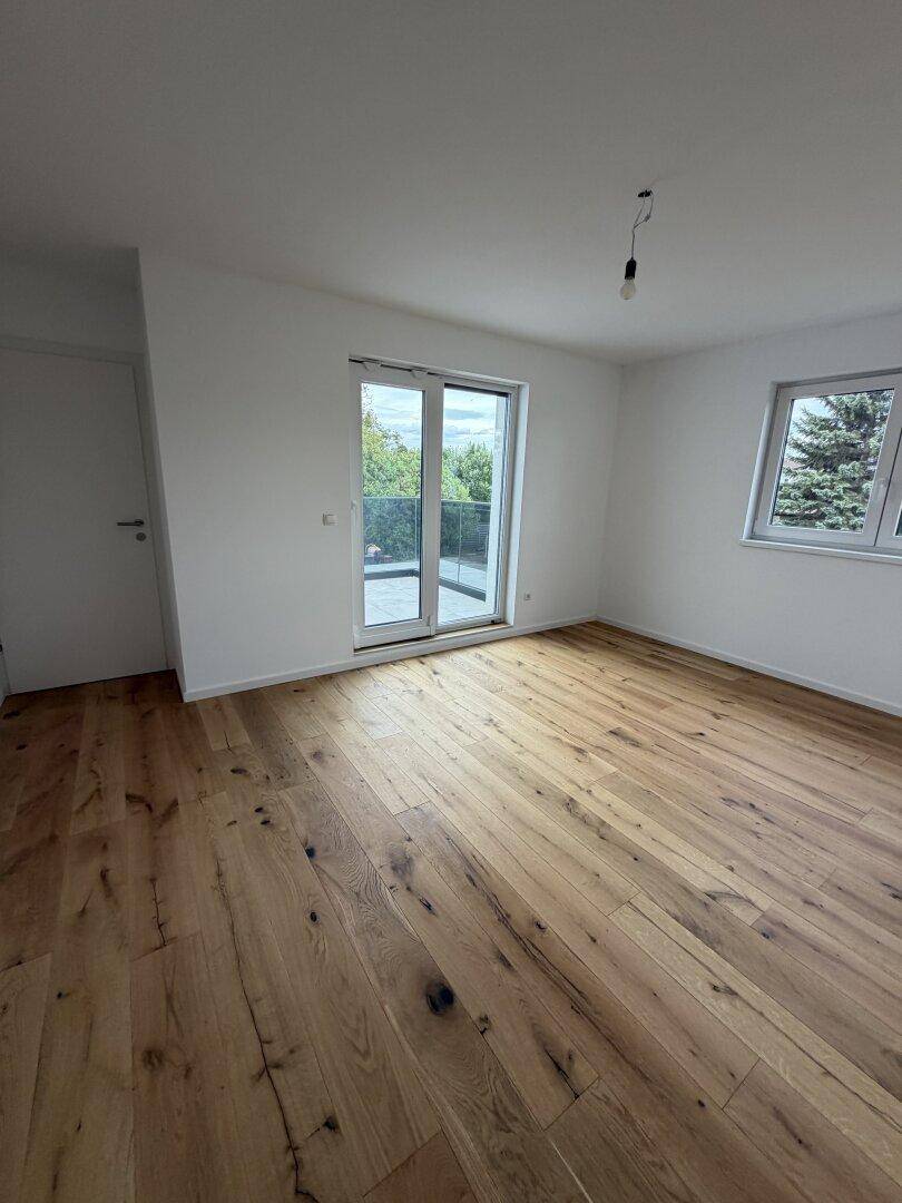 Heller Raum mit Holzdielenboden, Zugang zu einem Balkon und Blick ins Grüne.