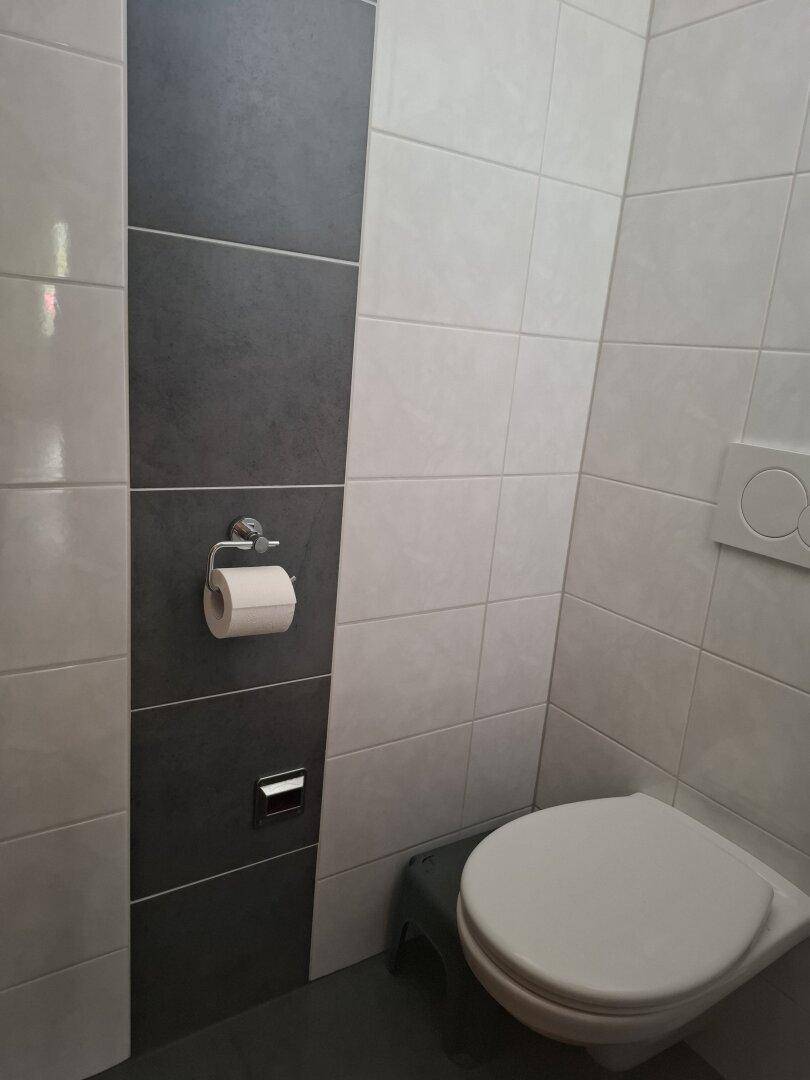 Modernes WC mit grauen und weißen Fliesen und wandhängender Toilette.