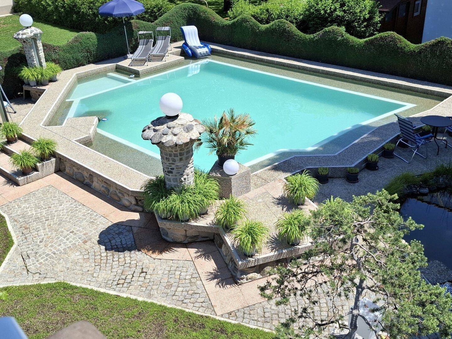 Vogelperspektive des Außenbereichs mit großem Pool, gepflasterten Wegen und Gartenlandschaft.